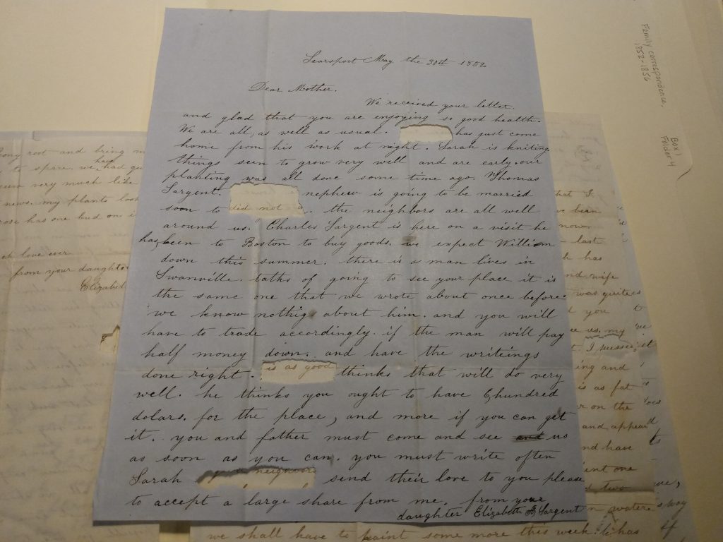 Color photograph of several black ink handwritten letters piled on top of each other. They have oval or rectangular ripped out sections, about the size of one word. 