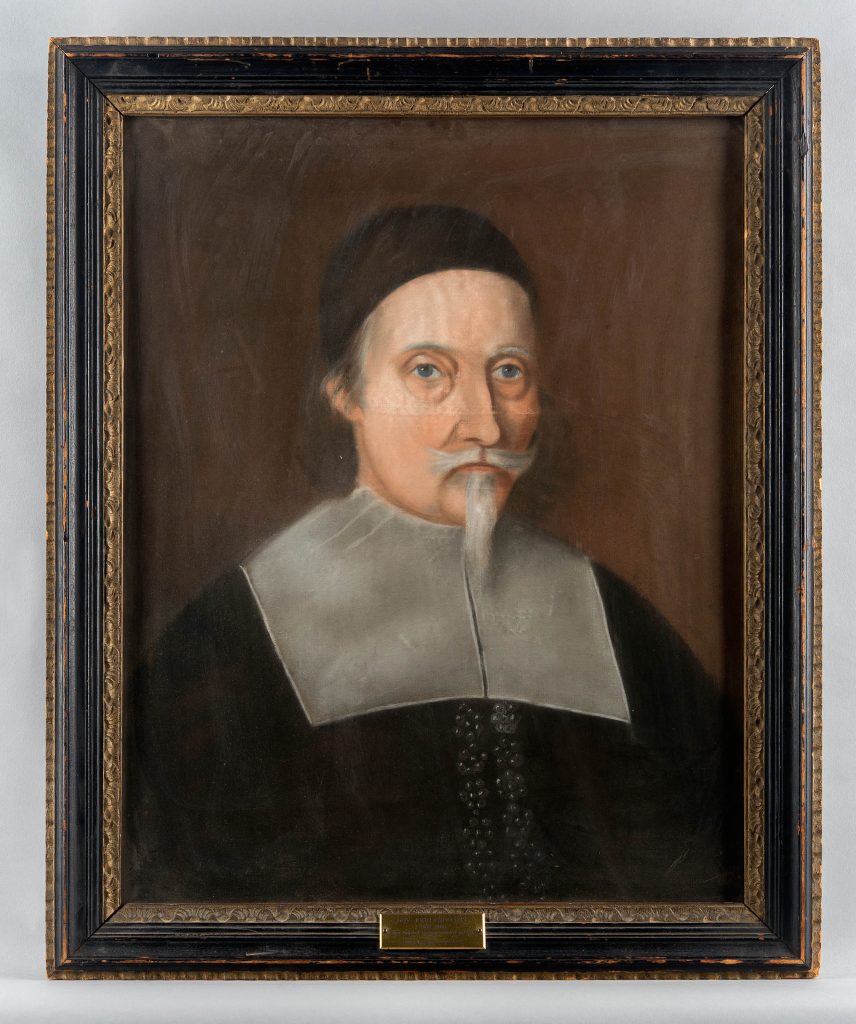 Portrait showing man in black cap with white beard against a black background