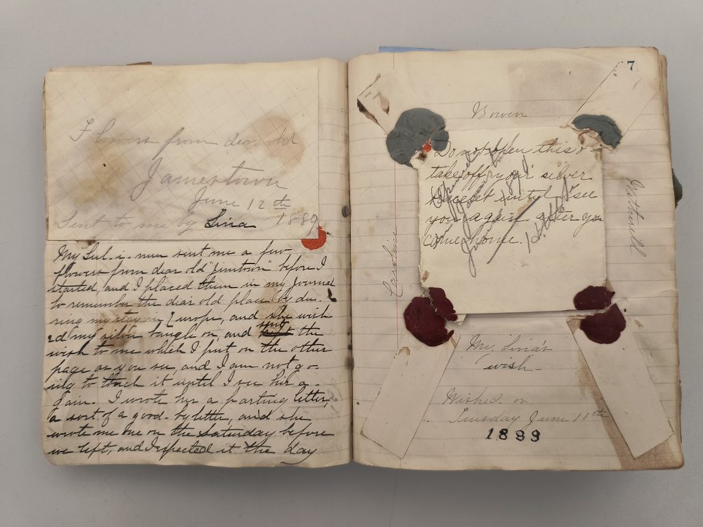 Color photograph of two pages of a volume. Attached to the left page is an envelope labeled in pencil, “Flowers from dear old Jamestown June 12th 1889 sent to me by Lina.” Below the envelope is more writing in black ink. Attached to the right page is a folded-up piece of paper, sealed by wax on four sides, and labeled in black ink, “Do not open this or take off your silver bracelet until I see you again after you come home.” The wax seals have been broken. Both pages are stained and discolored.