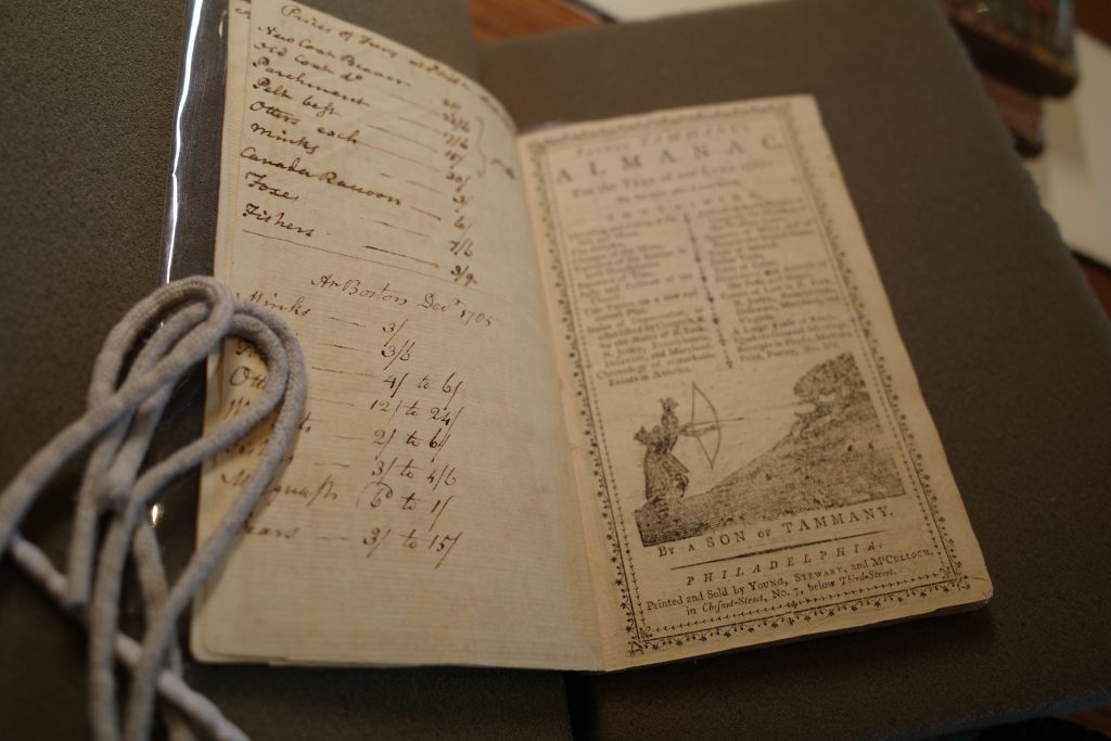 Photo of an open diary on a foam book cradle, with handwriting on left side and a printed page reading "Almanac" on the right side.