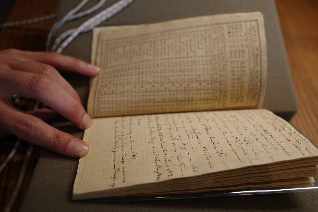 Photo of a diary open on a foam book cradle. A hand holds the pages open.